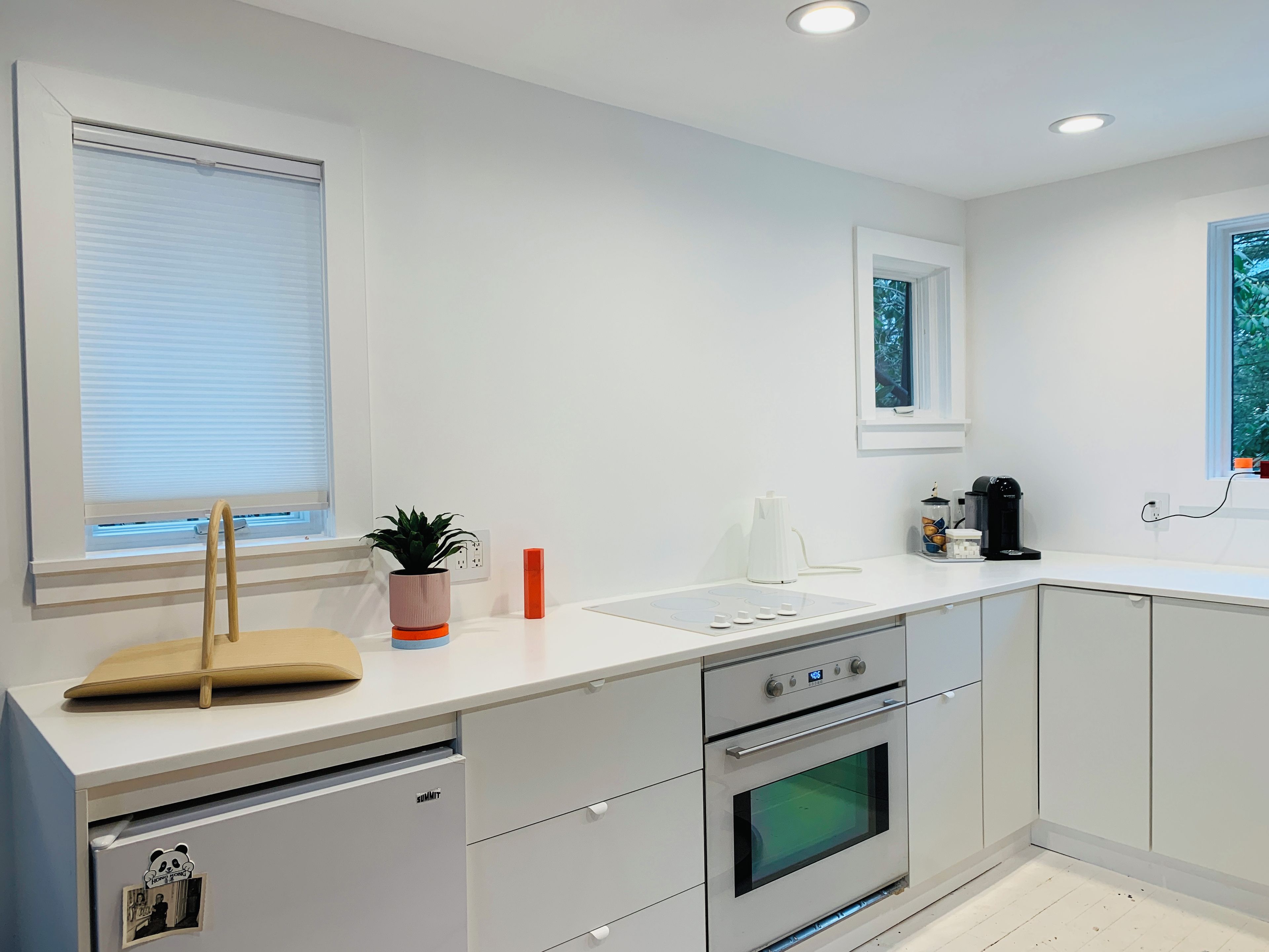 A modern kitchen with a built-in oven, a coffee maker, and a window with blinds.