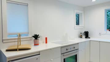 A modern kitchen with a built-in oven, a coffee maker, and a window with blinds.