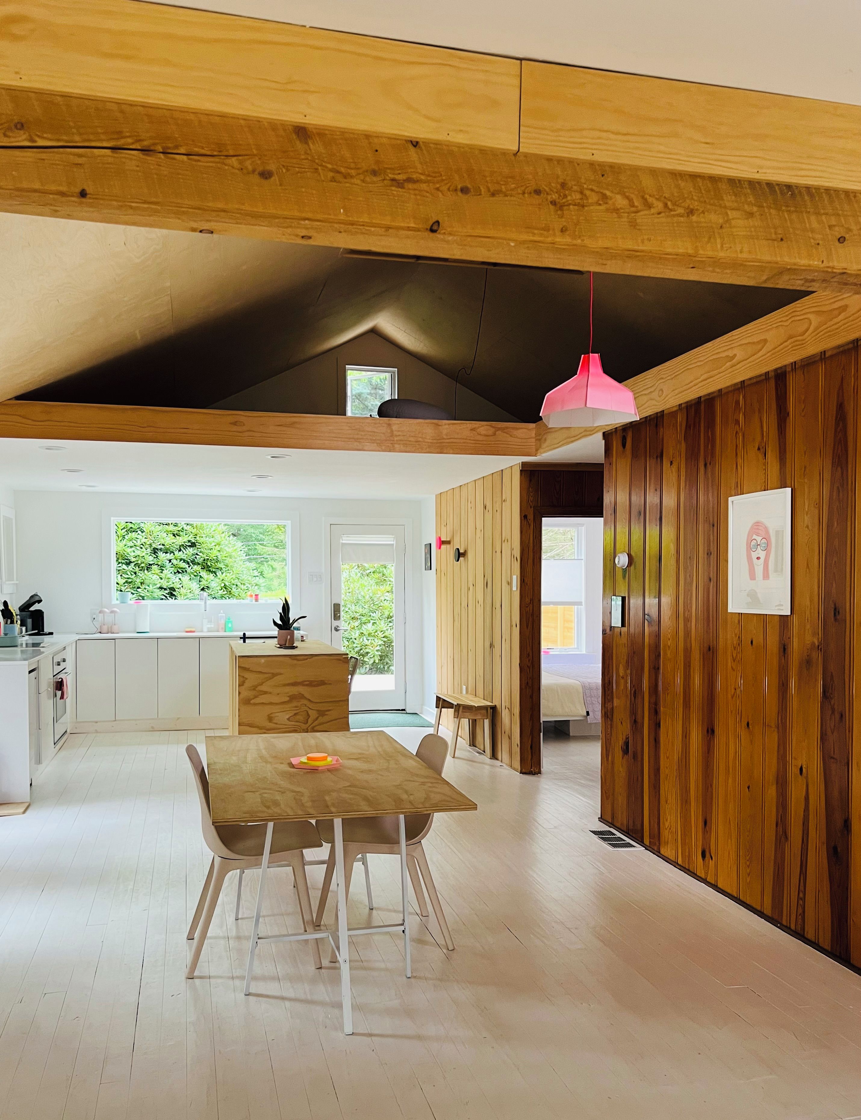 A spacious kitchen with a wooden ceiling, a dining area with a table and chairs, and a view of the outdoors through a window.