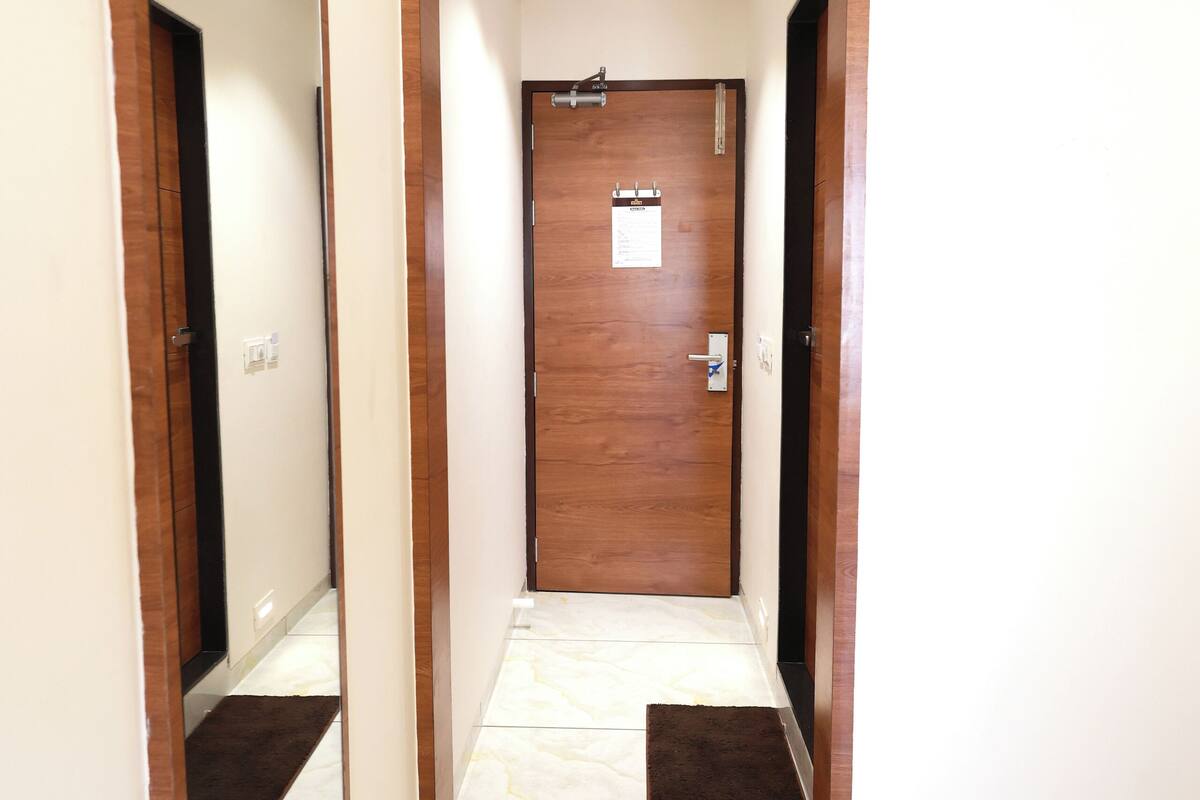 A hallway with a wooden door, a mirror on the left, and a small rug at the entrance.