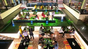 A dining area with multiple tables and chairs, a central water feature, and a patterned floor. - HOTEL GRAND HAVELI (Umargam)