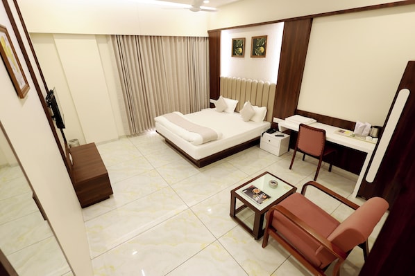 A hotel room with a bed, a desk, a chair, a small table, and a mirror.