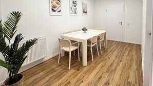 A dining area with a white table and chairs, a radiator, and three framed pictures on the wall. - House of Al-Ay Künzelsau (Künzelsau)
