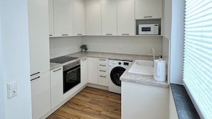 A compact kitchen with white cabinets, a built-in oven, a microwave, and a washing machine. - House of Al-Ay Künzelsau (Künzelsau)