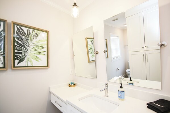 Une salle de bain avec un meuble-lavabo blanc, un grand miroir et des œuvres d’art encadrées accrochées au mur.