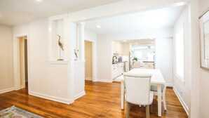 A spacious kitchen with white cabinets, a dining area with a white table and chair, and a wooden floor.