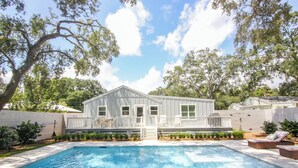 A house with a swimming pool, surrounded by trees and a white fence.