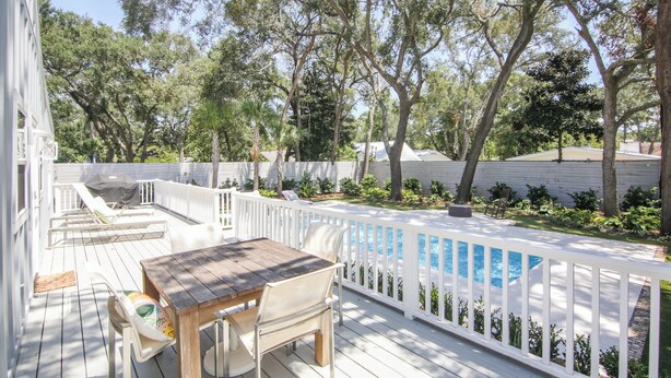 A wooden deck with a pool, white railings, and outdoor furniture.