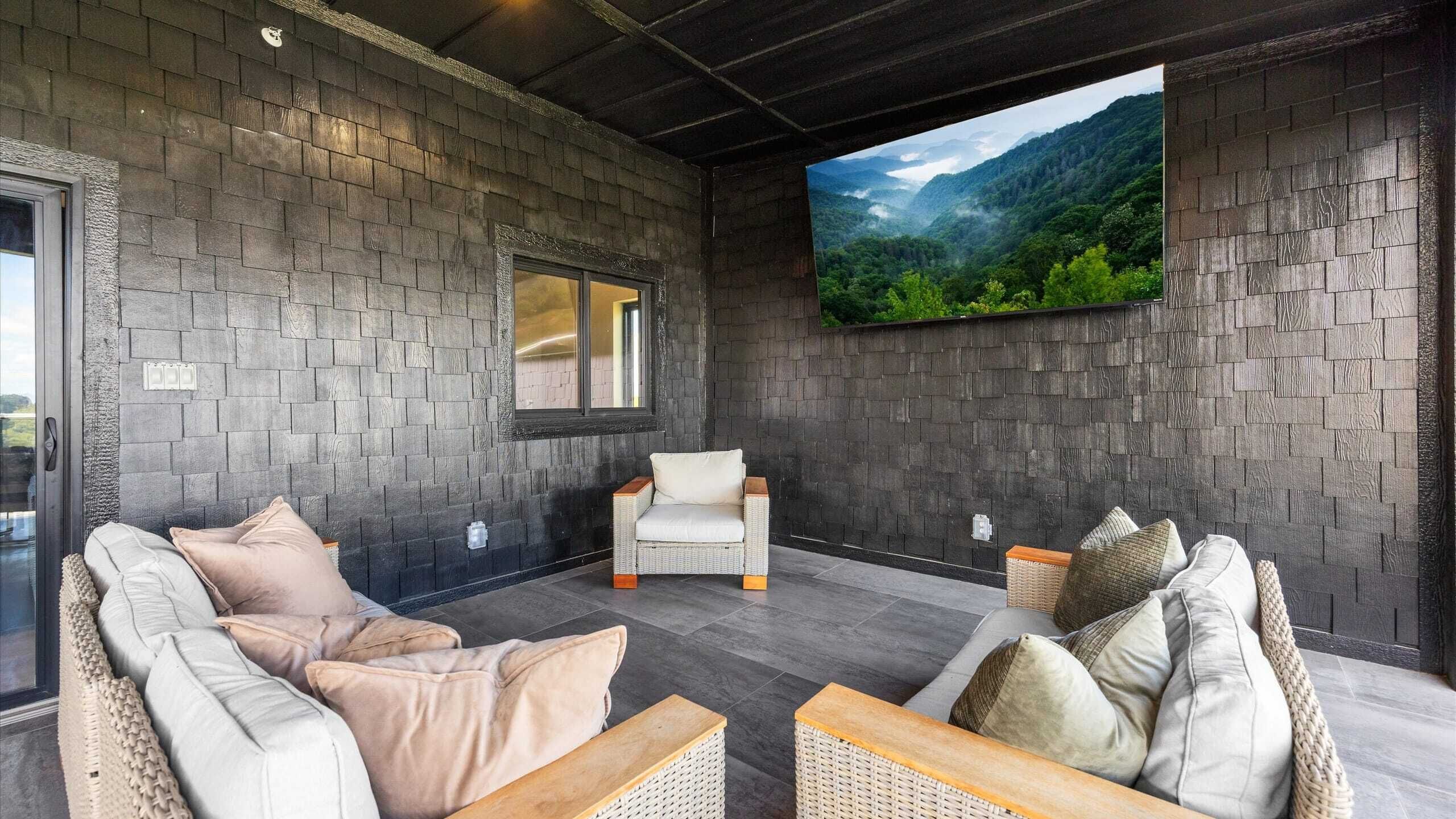 Ein moderner Lounge-Bereich mit dunklen Steinwänden, einem großen Flachbildfernseher und bequemen Sitzmöglichkeiten, darunter eine Couch und Sessel.