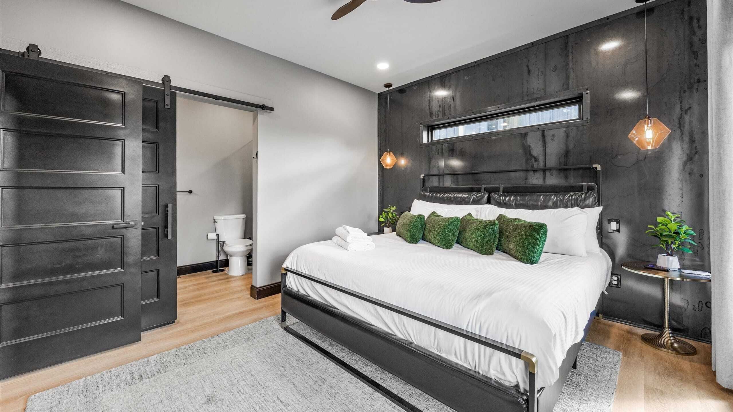 Une chambre à coucher moderne avec un lit, un plancher en bois, une grande armoire et une salle de bain visible à travers une porte ouverte.