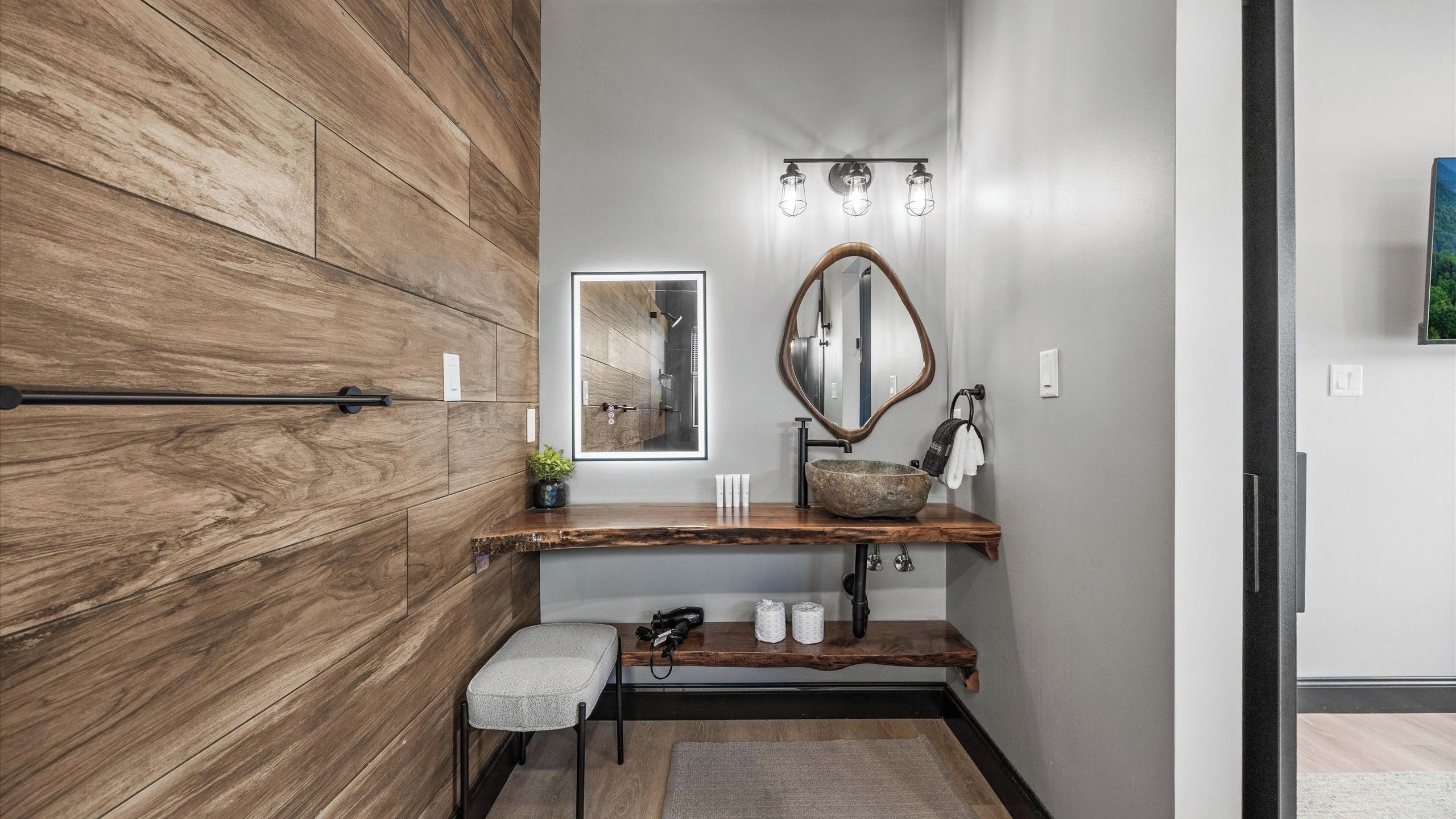 A modern bathroom with a wooden wall, a large mirror, a wooden vanity, a towel rack, and a shower.