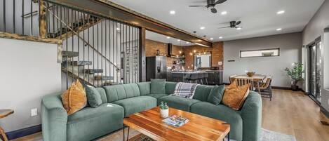 Een moderne woonkamer met een modulaire bank, een houten salontafel en een trap met metalen leuningen.