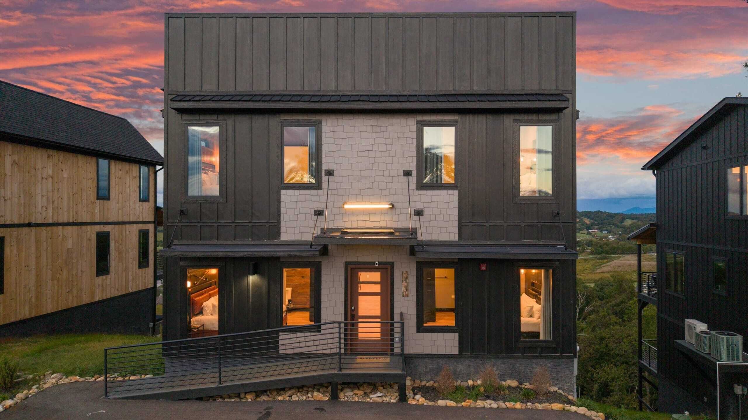 A modern two-story house with a prominent entrance, large windows, and a view of the surrounding landscape.