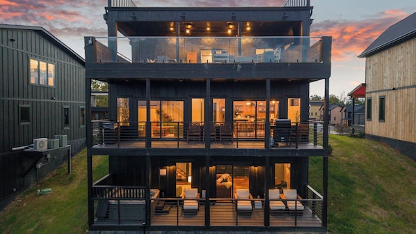 A multi-story building with a balcony, a kitchen area, and a seating area with chairs and a table.