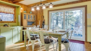 A dining area with a wooden table and chairs, a window with curtains, and a view of trees outside.