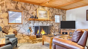 A stone fireplace with a fire, a television, and a leather sofa in a living room. - Lakefront w/ Private Dock, Hot Tub, Large Deck, Views Lakeside on Lagunita (Big Bear Lake)