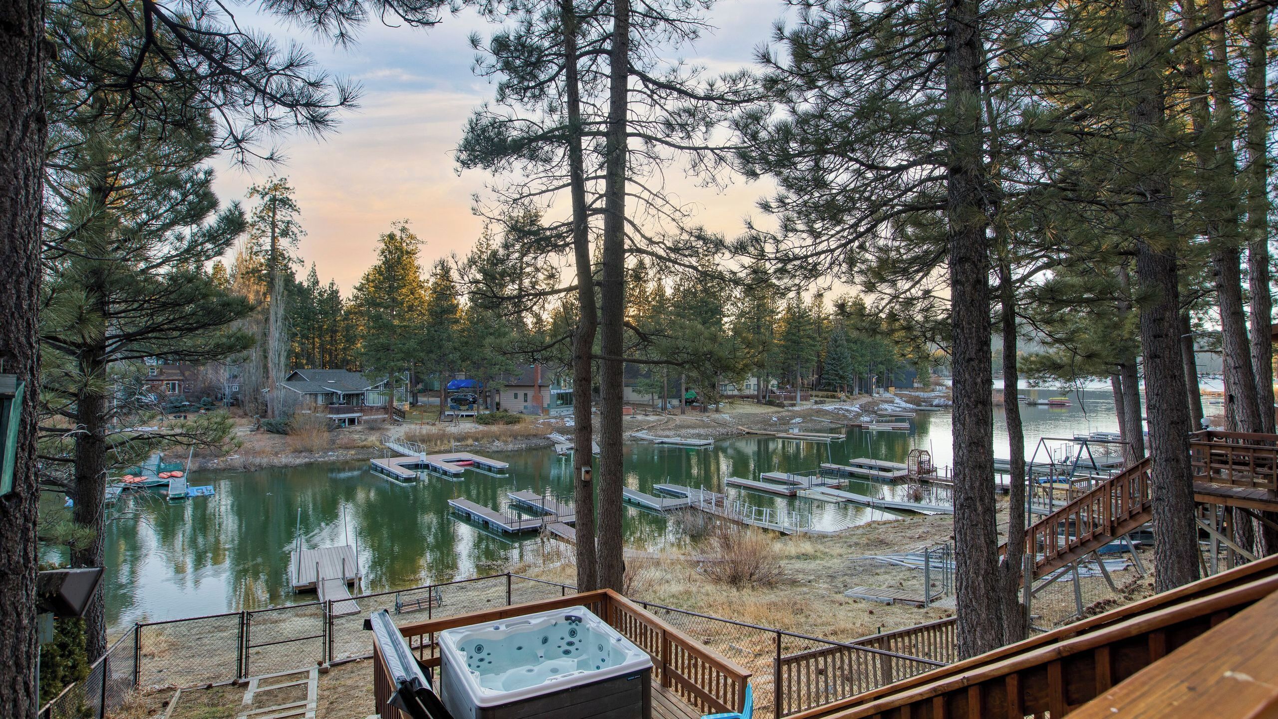 A lakeside property with a hot tub, docked boats, and a forested backdrop.