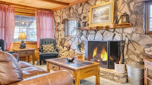A cozy living room with a stone wall, a fireplace, a leather sofa, and a wooden coffee table.
