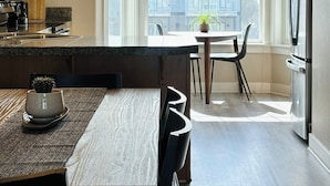 A modern kitchen with a central island, pendant lighting, and a view of residential buildings through large windows.