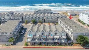 A coastal hotel with multiple-story buildings, a parking area, and a view of the ocean.