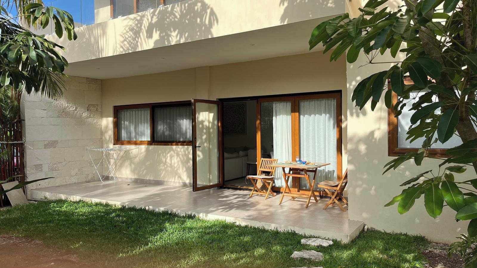 A modern house with a patio area featuring a table and chairs, large windows, and a grassy lawn.