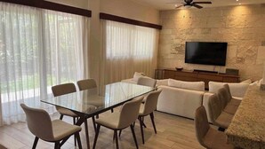 A modern living room with a glass dining table, beige sofas, and a stone wall with a flat-screen TV. - Beautiful apartment for rent Great location close to the beach, walking distance (Playa del Carmen)