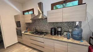 A modern kitchen with a gas stove, oven, microwave, and a coffee maker. There is a large water dispenser and a window above the sink. - Beautiful apartment for rent Great location close to the beach, walking distance (Playa del Carmen)