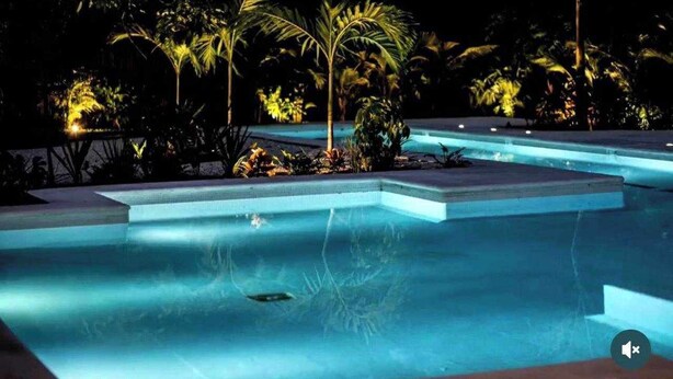 A swimming pool with steps leading into it, surrounded by palm trees and other tropical plants. - Beautiful apartment for rent Great location close to the beach, walking distance (Playa del Carmen)