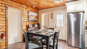 A log cabin interior with a dining area, a kitchen with a stainless steel refrigerator, wooden walls, and a painting on the wall. - HOT TUB, outdoor movie theater, coffee bar,Fire pit, BBQ, pavilion & LAKE VIEWS! (Greentown)