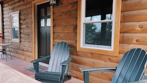 A wooden cabin with two Adirondack chairs on a porch, a door, and a window with a sign. - HOT TUB, outdoor movie theater, coffee bar,Fire pit, BBQ, pavilion & LAKE VIEWS! (Greentown)