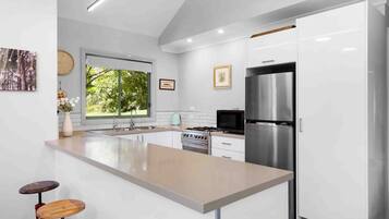 A modern kitchen with a central island, stainless steel appliances, and a view of greenery outside.