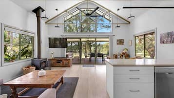 A spacious kitchen with a large island, wooden flooring, and a view of the outdoors through large windows.