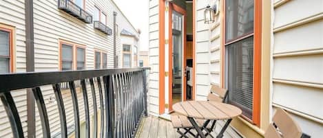 A balcony with a table and chairs, a railing, and a building with windows and a door.