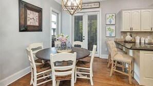 A dining area with a round table, white chairs, and a chandelier. - 7-bedroom cottage in fabulous St. Simons Island with lounge pool, WiFi, AC. (St. Simons Island)