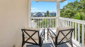 A balcony with two chairs and a table, overlooking a residential area with houses and greenery. - 7-bedroom cottage in fabulous St. Simons Island with lounge pool, WiFi, AC. (St. Simons Island)