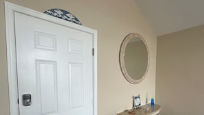 A hallway with a white door, a small sink with a mirror, and a trash bin.