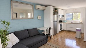A compact living space with a sofa, a dining table, a kitchen area, and a large mirror. - Blue Waters - Scarborough 1bed (Scarborough)