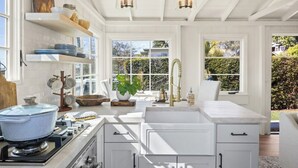 A kitchen with white cabinetry, a stove, and a sink. There are shelves with dishes and a potted plant. -  Avail  this Dec 1st  2026. (Laguna Beach)