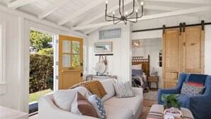 A cozy living room with a white sofa, blue armchair, and a wooden door. -  Avail  this Dec 1st  2026. (Laguna Beach)