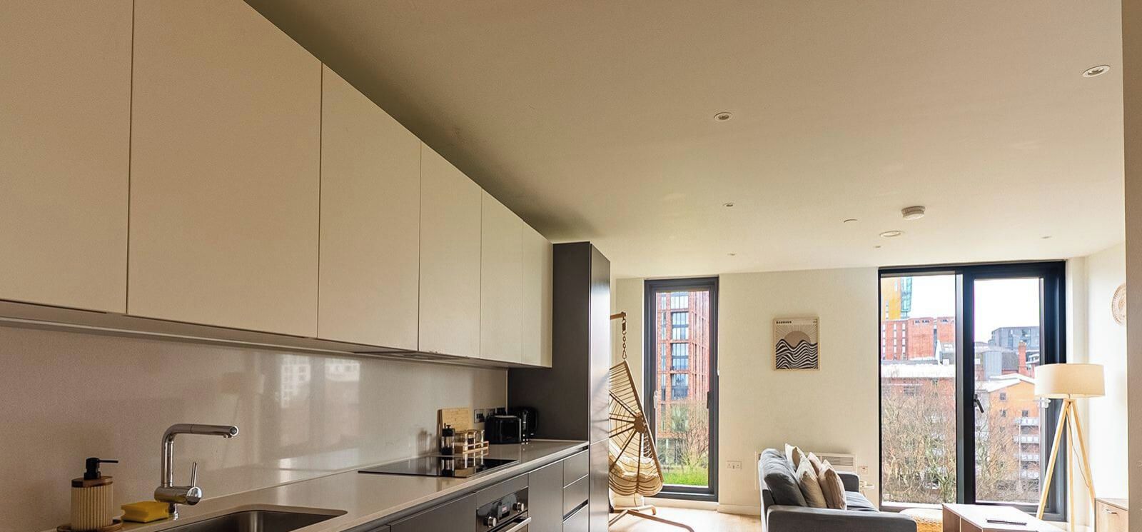 Eine moderne Küche mit Einbauherd, Spüle und Schränken. Es gibt einen Essbereich mit einer Couch und einer Lampe.