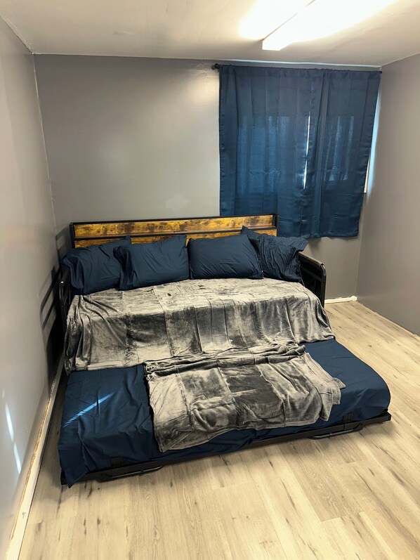 Une pièce avec un lit, une fenêtre avec des rideaux et un plancher en bois.