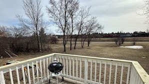 A wooden deck with a grill, surrounded by bare trees and a grassy field.