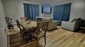 A dining area with a wooden table and chairs, a sofa, and a television mounted on the wall.