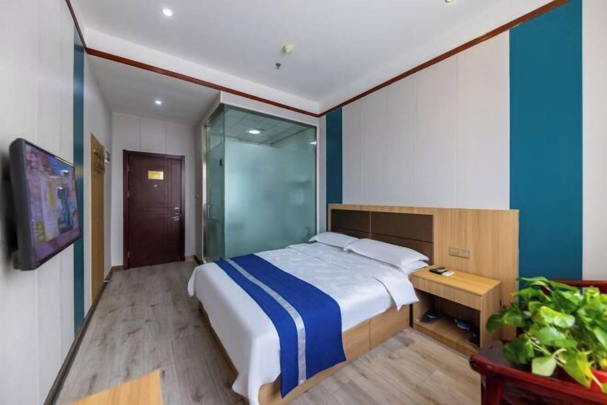 A hotel room with a bed, bedside table, and a potted plant.