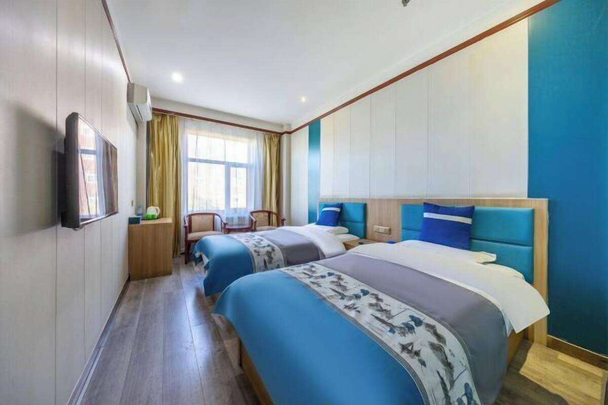 A hotel room with two beds, a desk, a chair, and a TV.