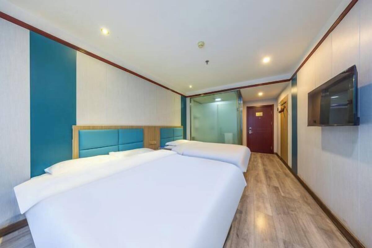 A hotel room with two beds, a television on the wall, and a wooden floor.
