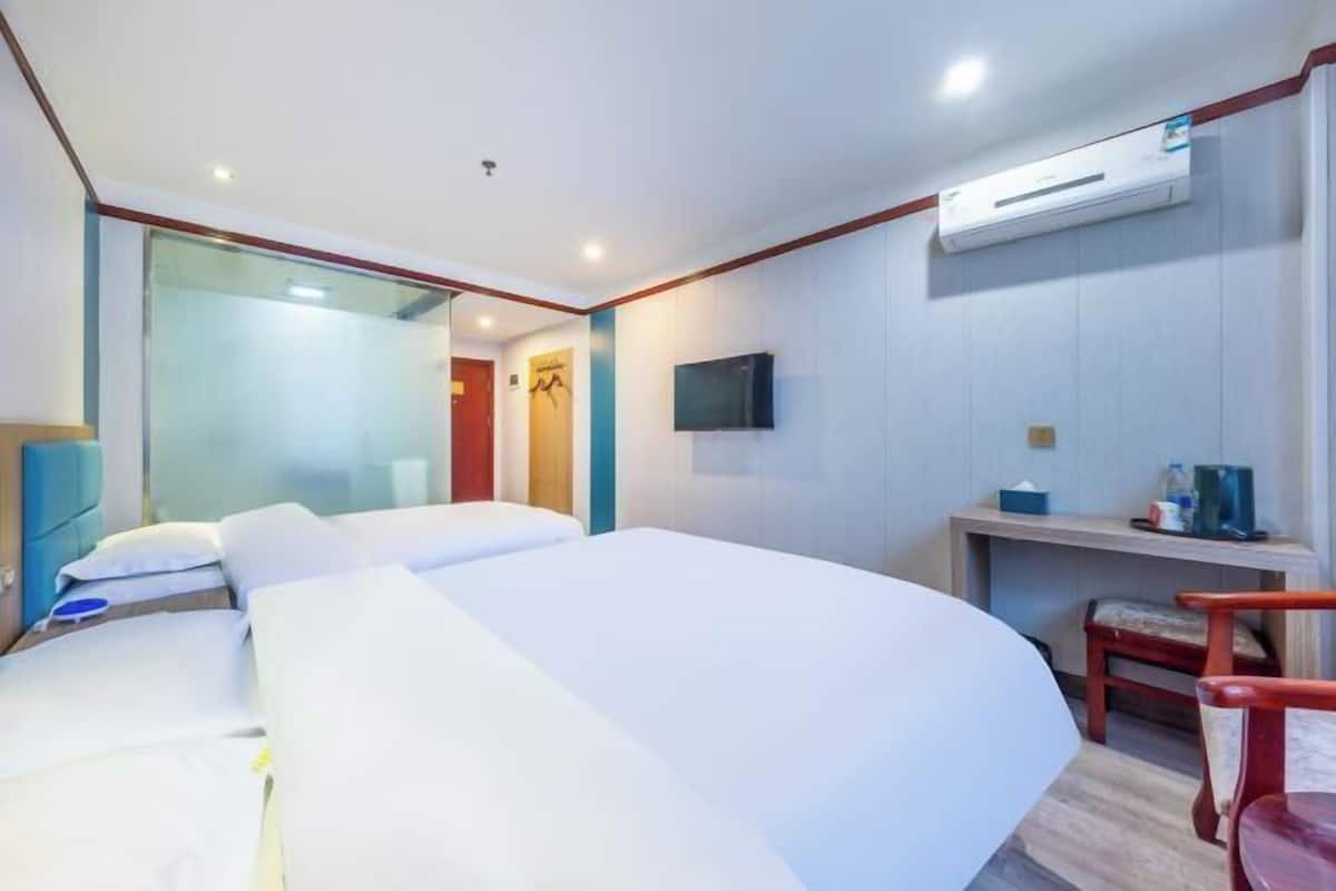 A hotel room with a large bed, a desk, a chair, a TV, and an air conditioning unit.