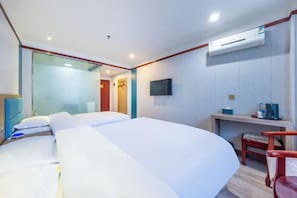 A hotel room with a large bed, a desk, a chair, a TV, and an air conditioning unit.