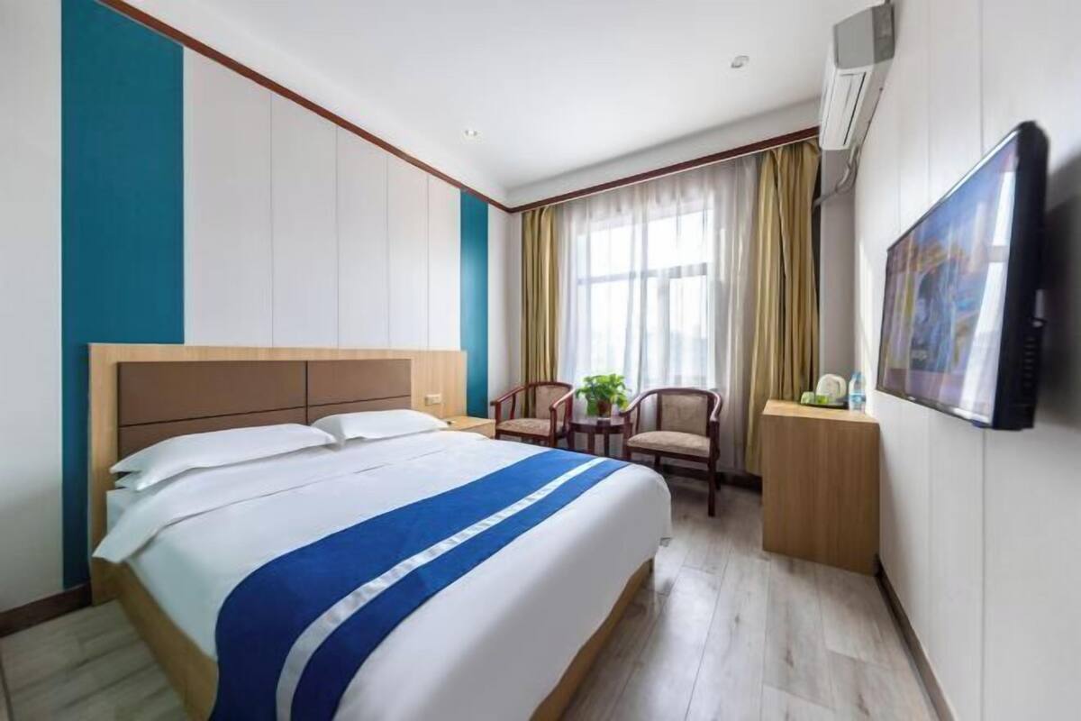 A hotel room with a large bed, a desk with a chair, a television, and a window with curtains.