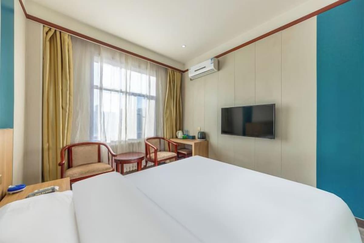 A hotel room with a large bed, a desk with a chair, a television mounted on the wall, and a window with curtains.